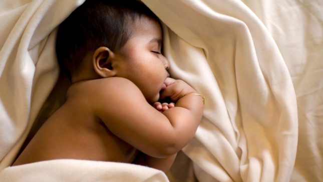 Baby sleeping calmly in an ivory blanket without any symptoms of Infant Shudder Syndrome 