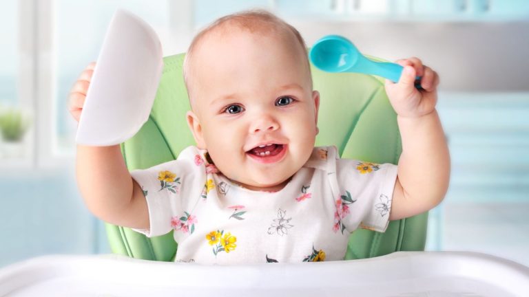 Excited baby ready to eat Puffs, holding a plate and a spoon in the air